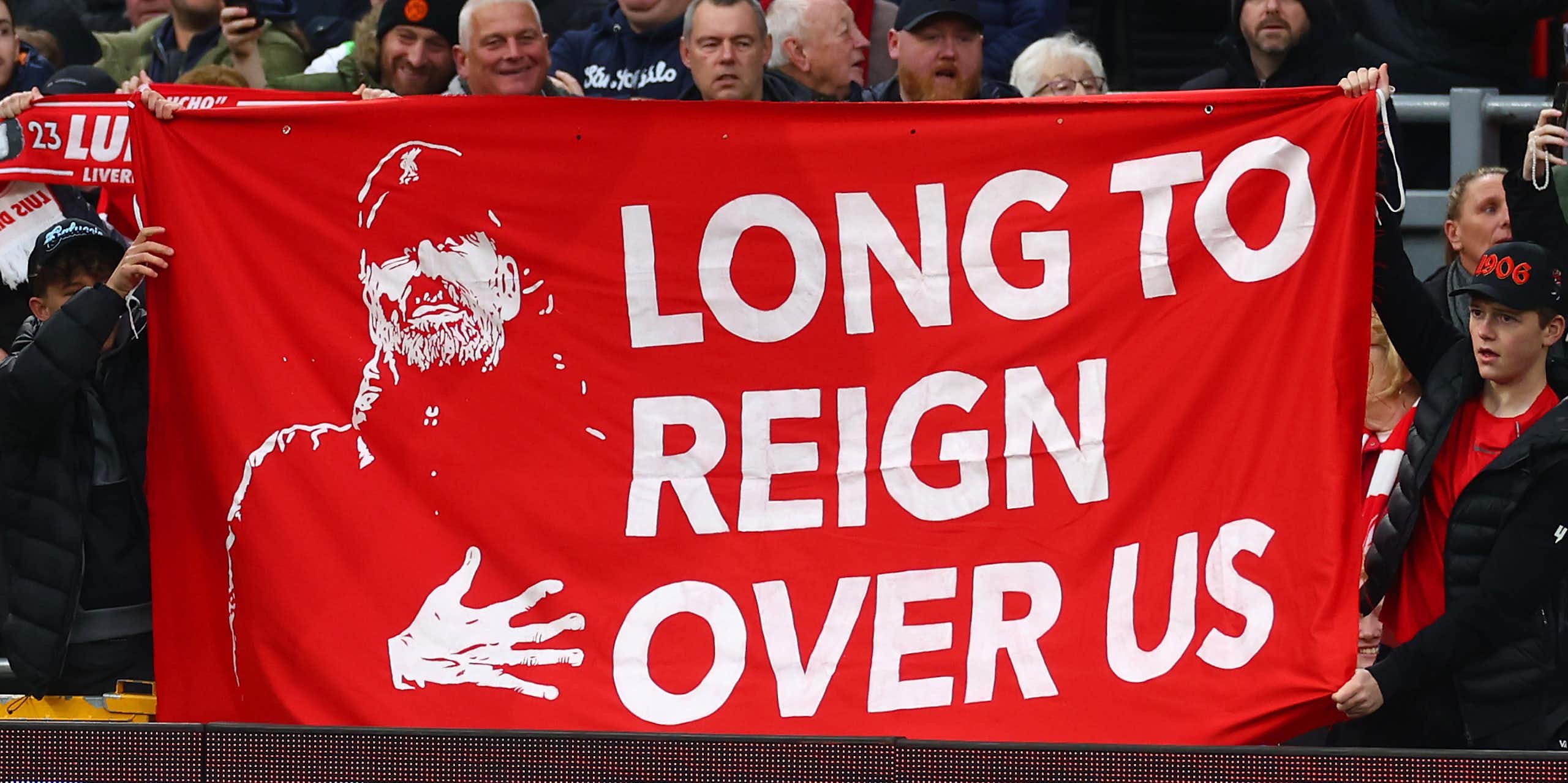 A group of Liverpool FC supporters hold up a large red and white banner depicting an image of manager Jurgen Klopp and the words 'Long to reign over us'