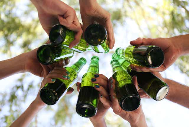 Photo from below of a group of hands toasting with green beer bottles