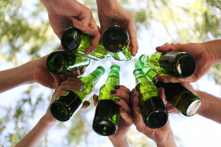 Photo from below of a group of hands toasting with green beer bottles