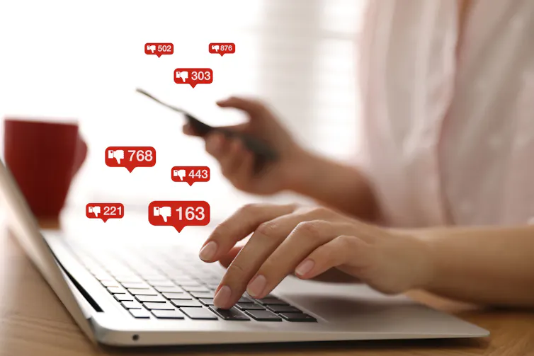 Hand hovering over keyboard surrounded by social media dislike buttons.