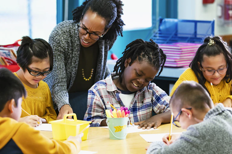 Teacher leans over elementary school students working at table