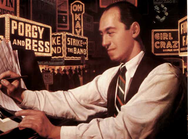 Painting of balding man wearing a white shirt and a tie, sitting at a piano and writing on sheets of music.