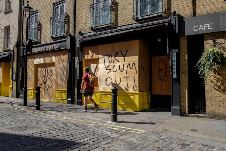 A boarded up shop on which someone has graffitied 'Tory Scum Out'.