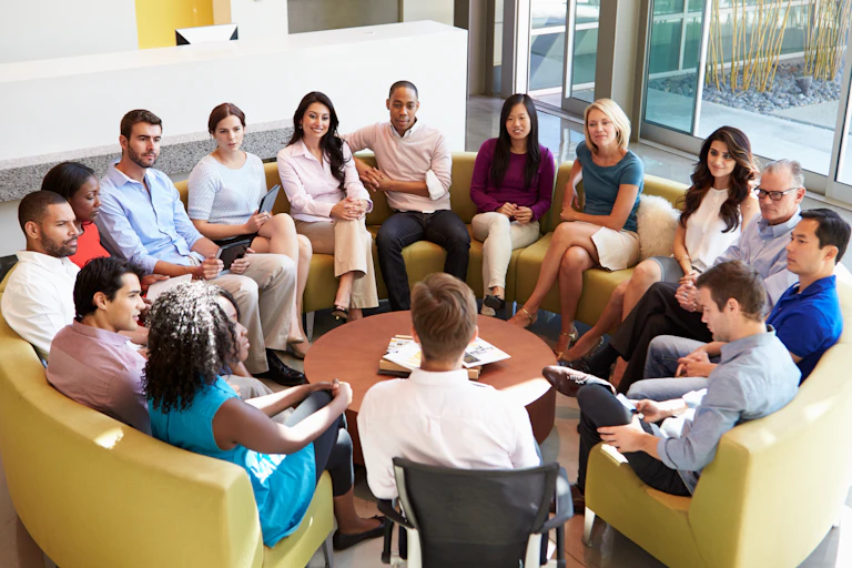 A group of 15 people sitting on a circular sofa and having a conversation