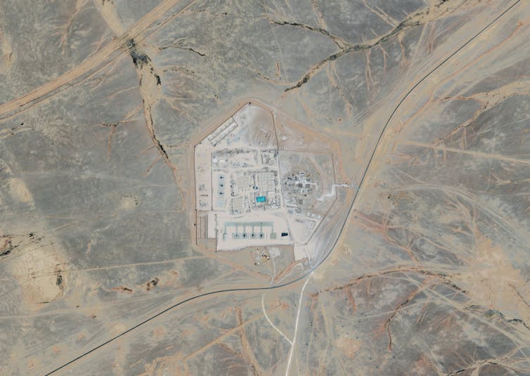 A satellite image shows a cleared area in a desert with beige and grey buildings, seen from high in the sky