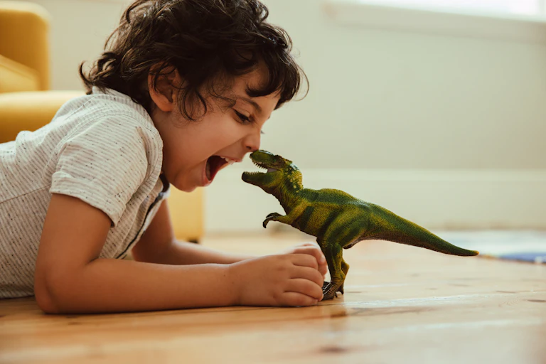Anak laki-laki bermain dengan mainan T-Rex di lantai