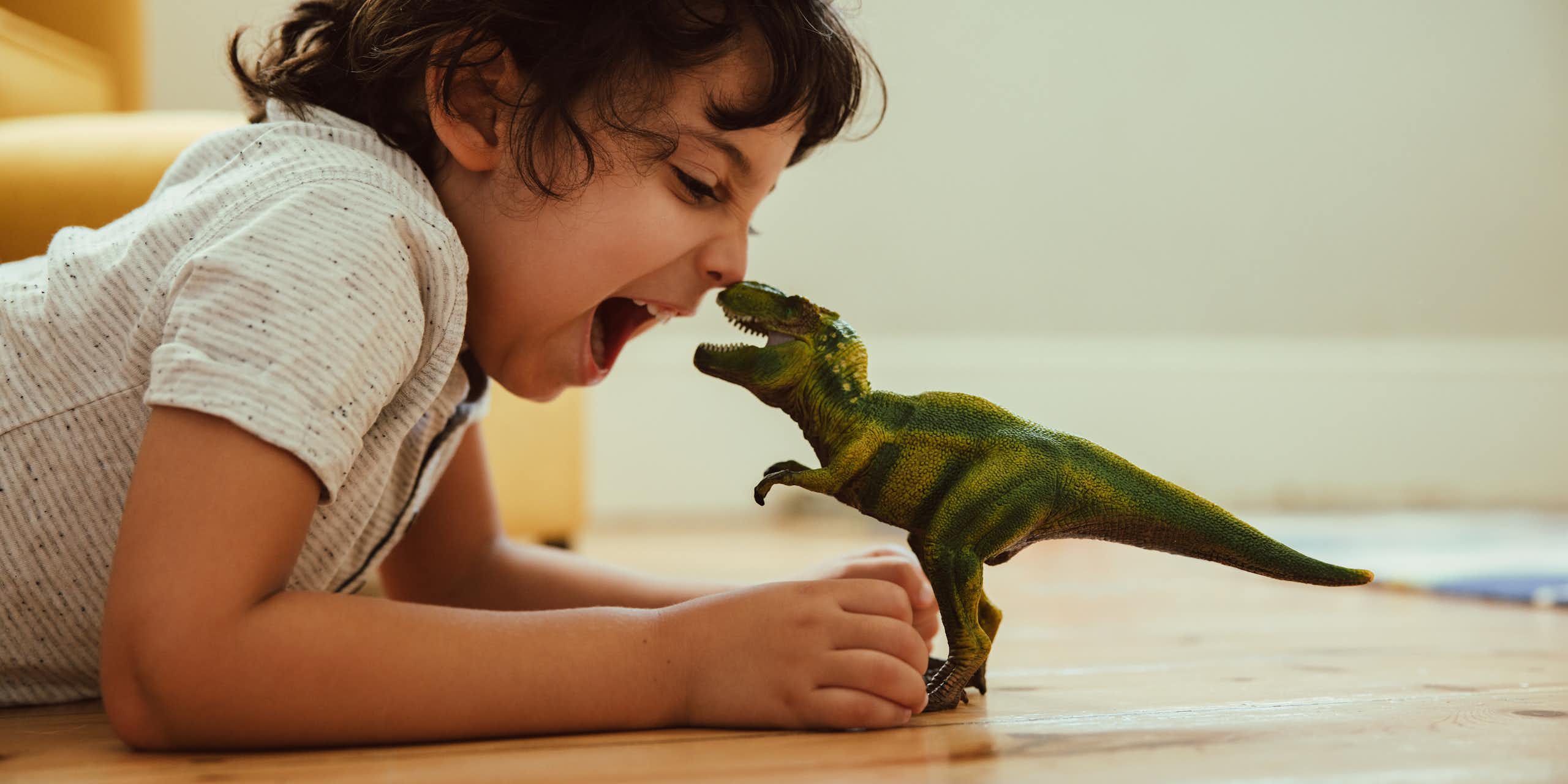 Anak laki-laki bermain dengan mainan T-Rex di lantai