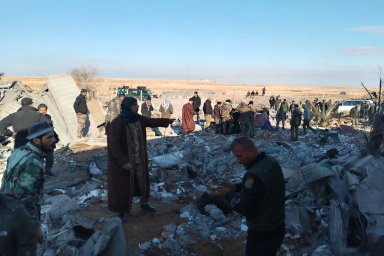 A group of men stand amid rubble.