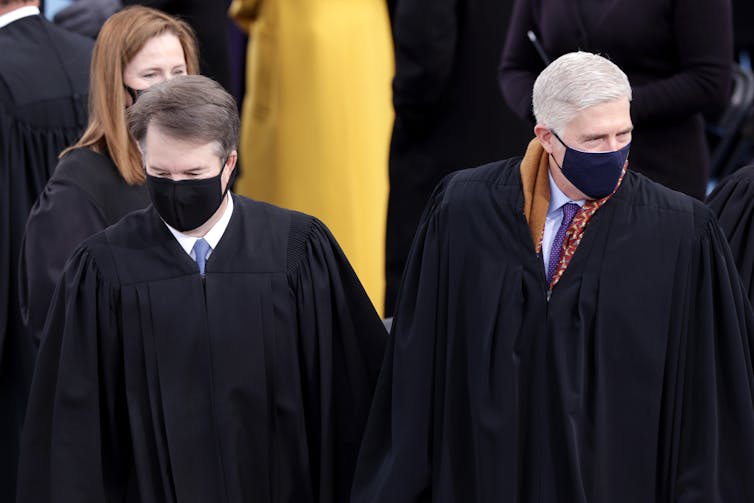Three people wearing black robes and masks.