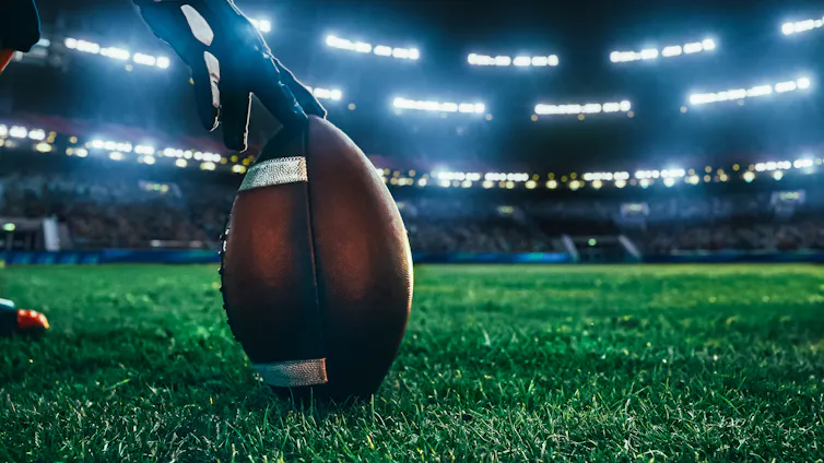 Une main gantée tient un ballon de football sur une surface gazonnée
