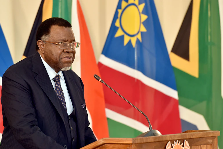A man speak at a podium with the Namibian and South African flags in the background.