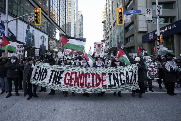People walk down a city street carrying a banner that reads End the Genocide in Gaza.