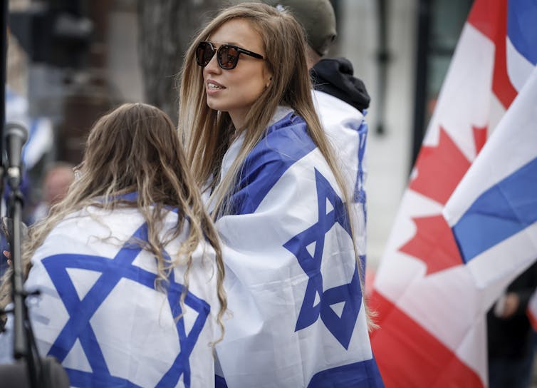 A woman and child are wrapped in the flag of Israel with a Canadian flag behind them.