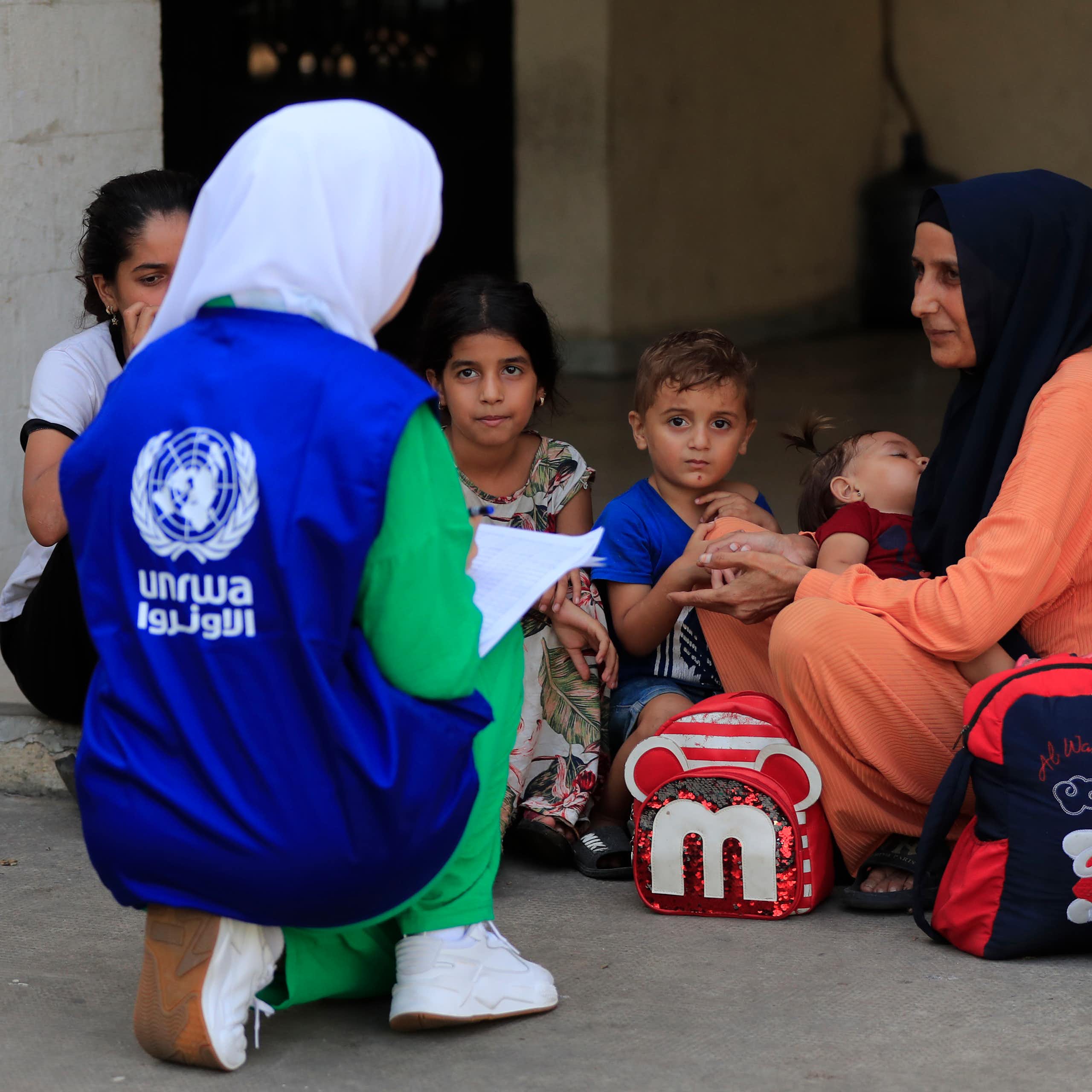 A woman wearing a blue UNRWA vest speaks to a woman with young children.