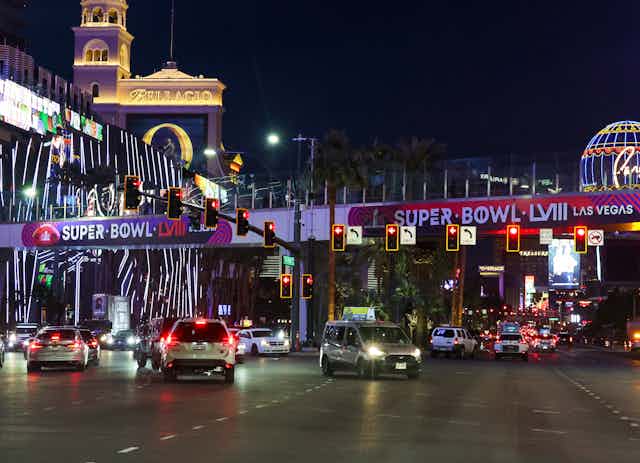 Wide boulevard in Las Vegas at night with flashy billboards and signs advertising the Super Bowl.