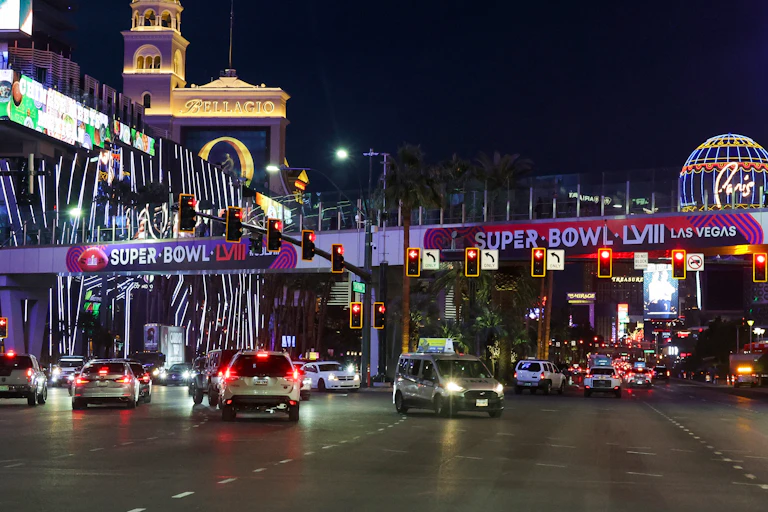 Wide boulevard in Las Vegas at night with flashy billboards and signs advertising the Super Bowl.