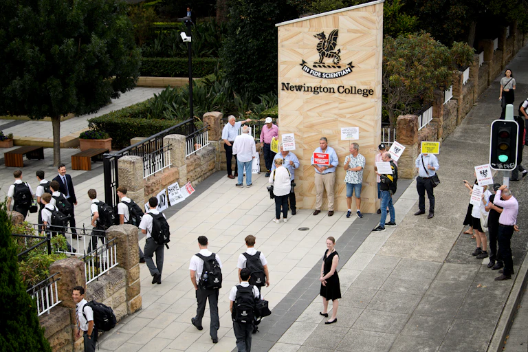 Students walk through the gates of Newington, as protestors hold signs against the school's plans to go co-ed.