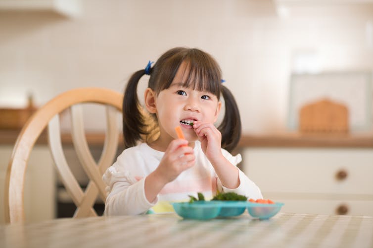 A young girl eats vegetables.