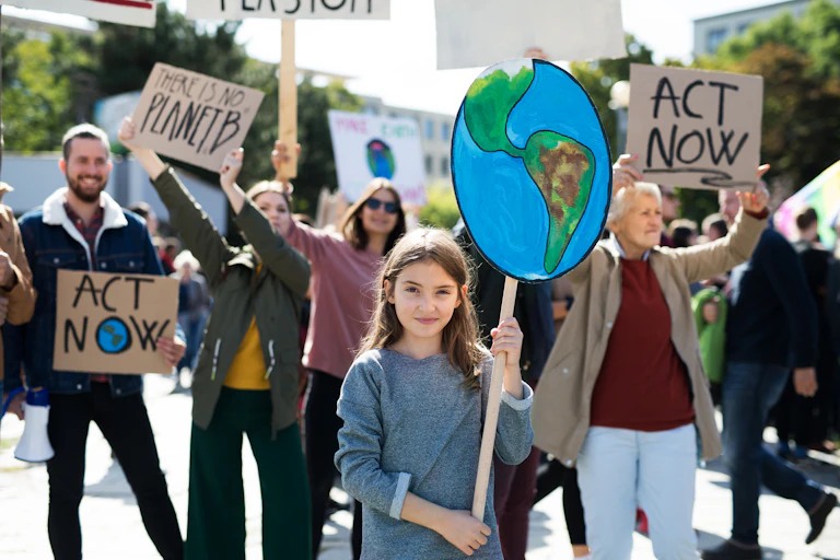 A brunette girl holds a poster of part of the Western Hemisphere during a protest on a street.