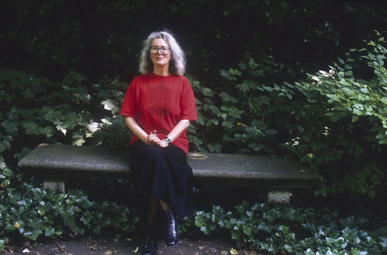 Novelist Angela Carter sitting on a park bench.