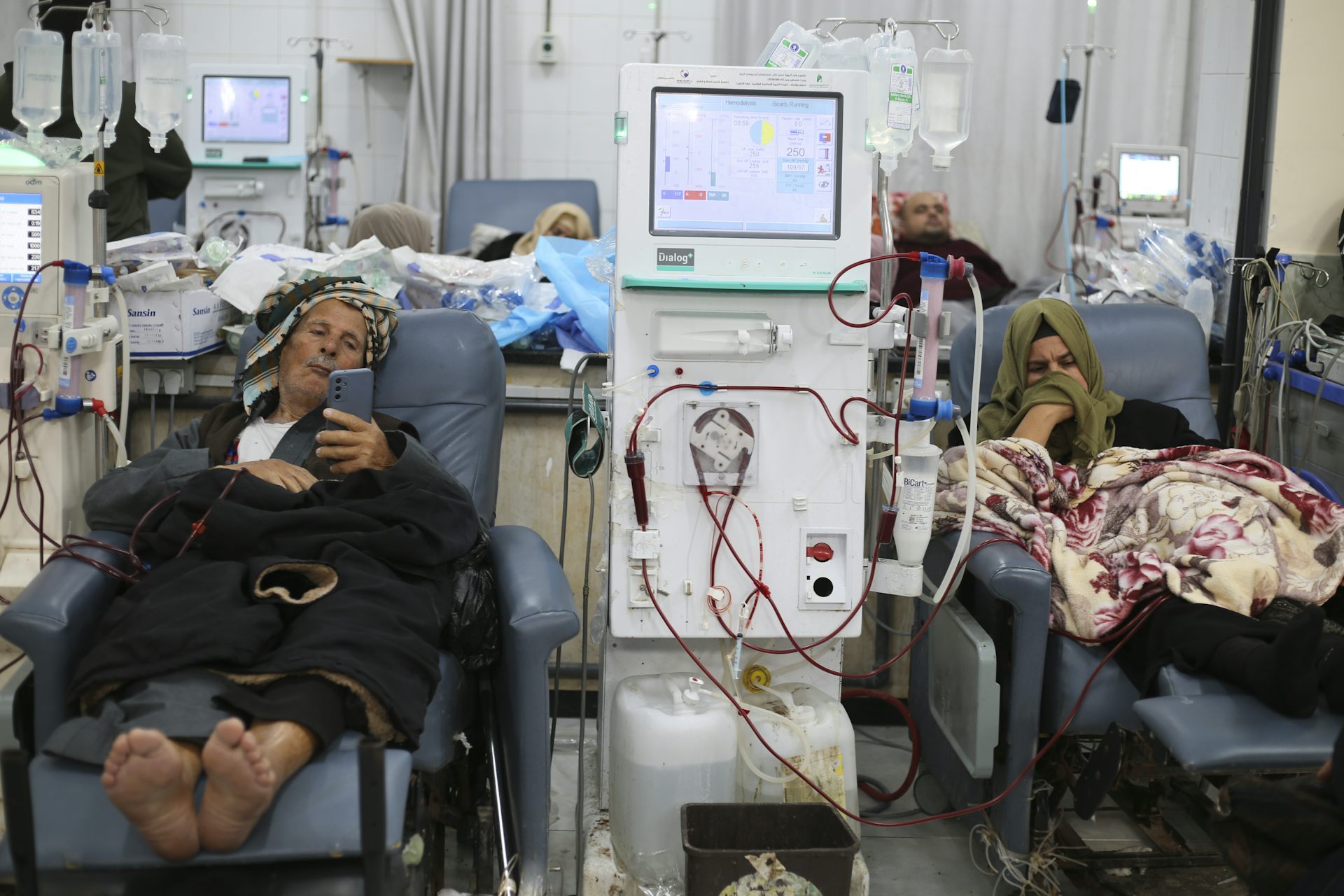 A man and a woman lying in treatment beds on either side of a dialysis machine