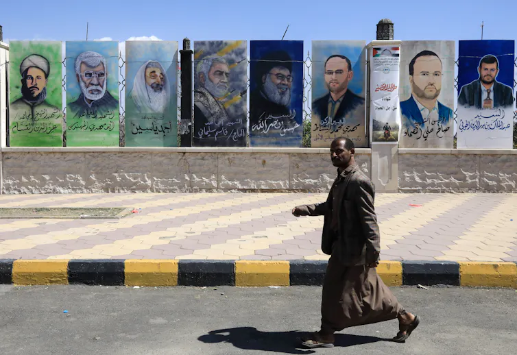 Man walks past a wall with portraits of leaders of Iran-sponsored armed groups in the Middle East.
