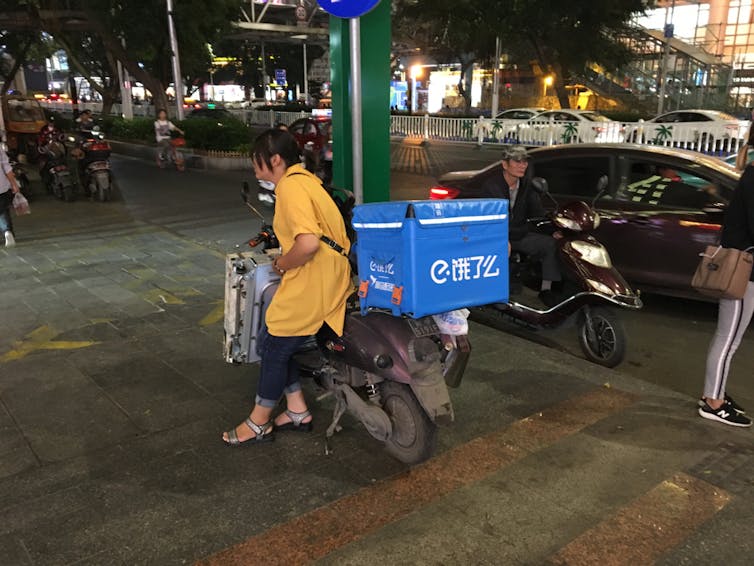 Female delivery rider standing beside her scooter