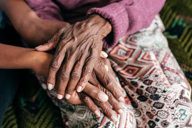 Closeup of an elderly person's hands, clasping a younger person's hands.