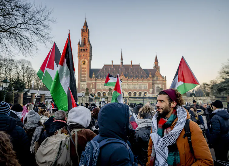 Crowd of people wearing winter clothing carrying Palestinian flags.
