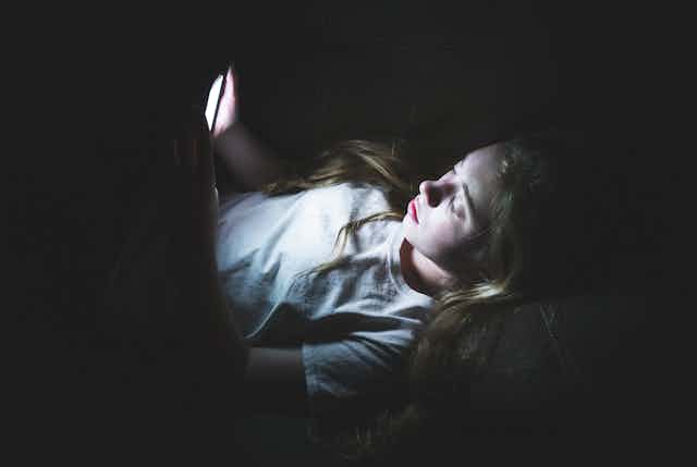 Una adolescente observa la pantalla de su móvil en una habitación a oscuras.