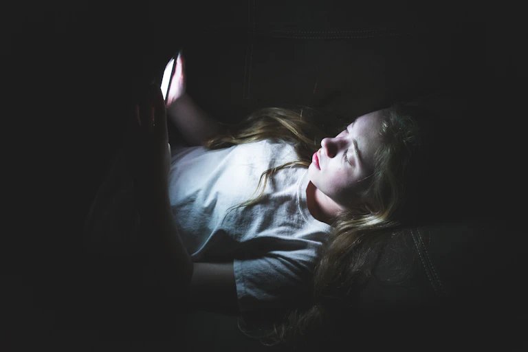 Una adolescente observa la pantalla de su móvil en una habitación a oscuras.