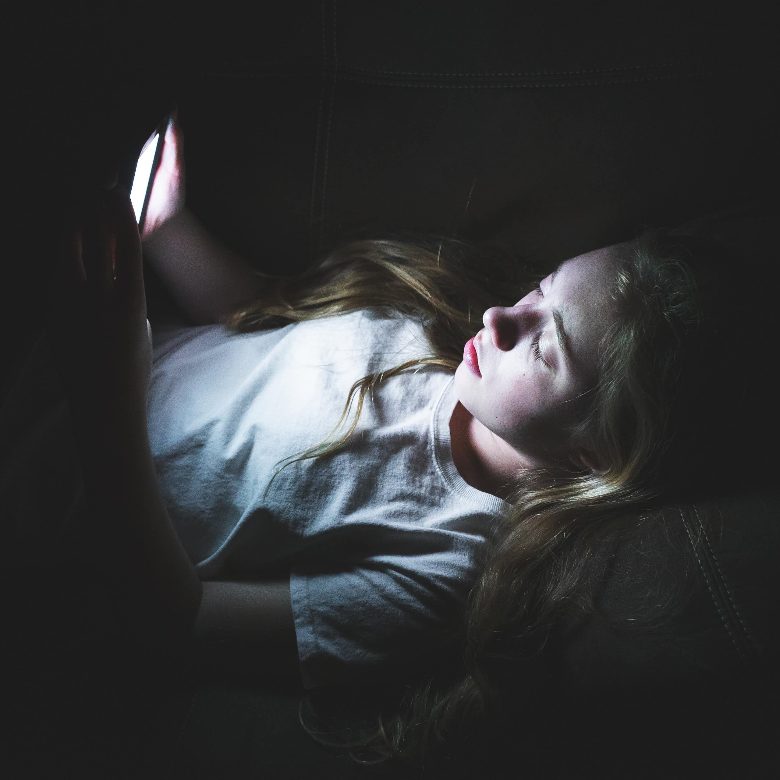 Una adolescente observa la pantalla de su móvil en una habitación a oscuras.