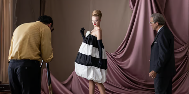 A woman in a very fancy black and white dress being photographed in a studio while the designer looks on.