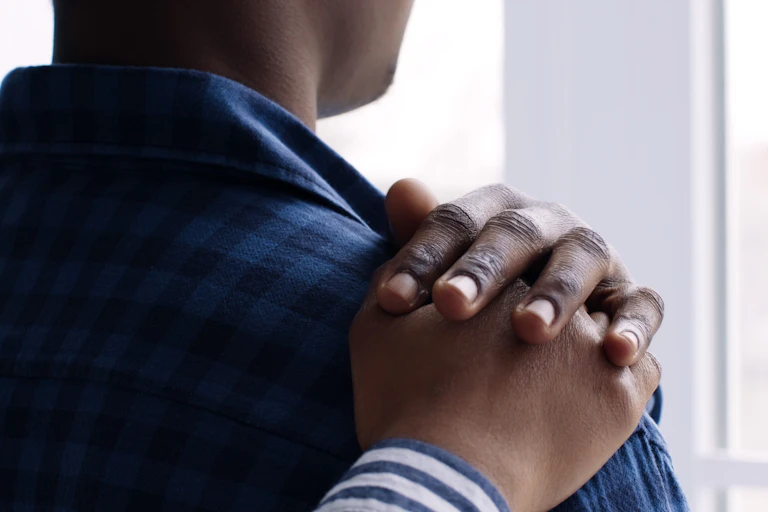 A hand on the shoulder of a black man who is looing out of a window