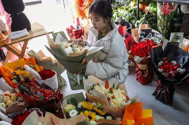 A young woman holding a bouquet of flowers while standing in a shop, surrounded by colorful bouquets ready to be sold.