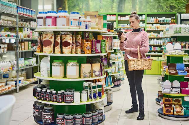 Young woman reading the label on a supplement product in a health food store.