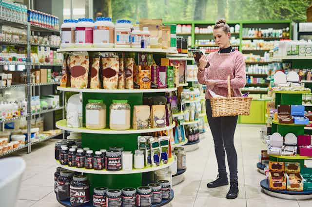 Young woman reading the label on a supplement product in a health food store. 