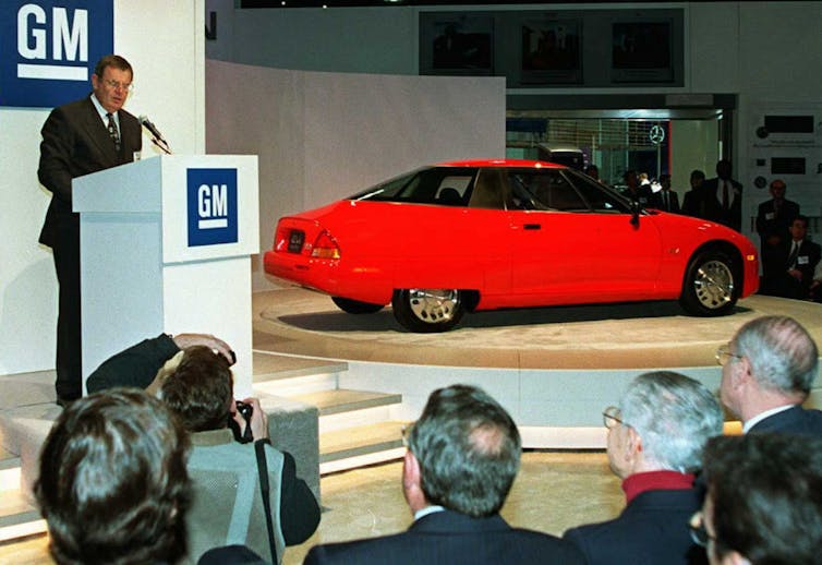In a 1996 photo, the chairman of General Motors shows the new EV1 electric passenger car to a gaggle of reporters.