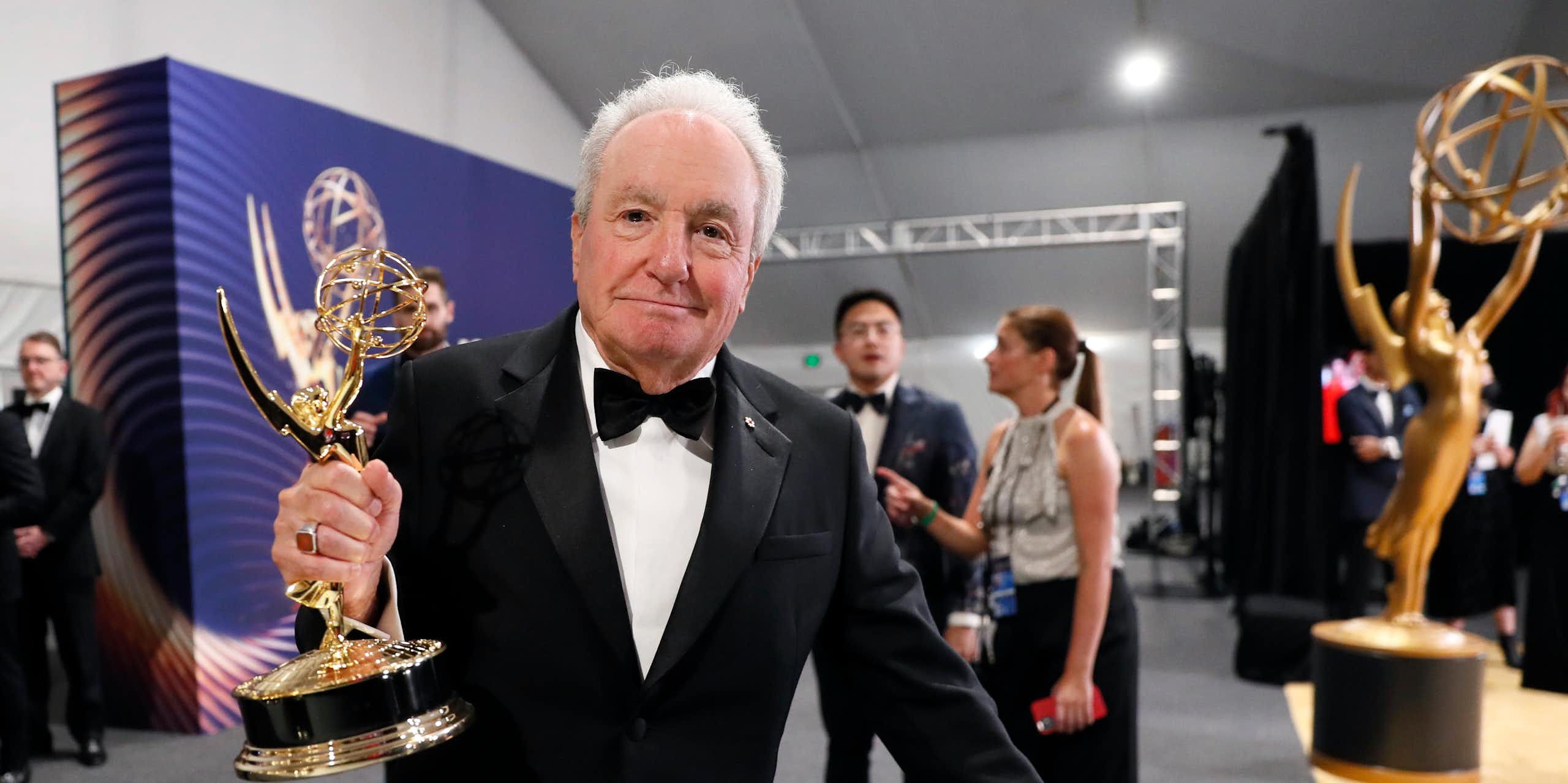 White-haired man in a tuxedo holds an Emmy award