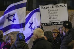 A woman holds up an Expel UNRWA sign amid Israeli flags.
