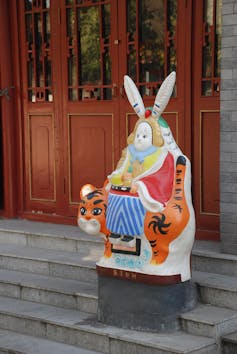 Statue of a human figure with a rabbit's head, seated on a tiger