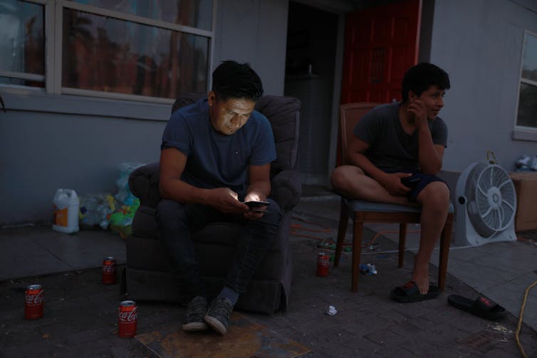 Two men look at cell phones in the dark on a porch.