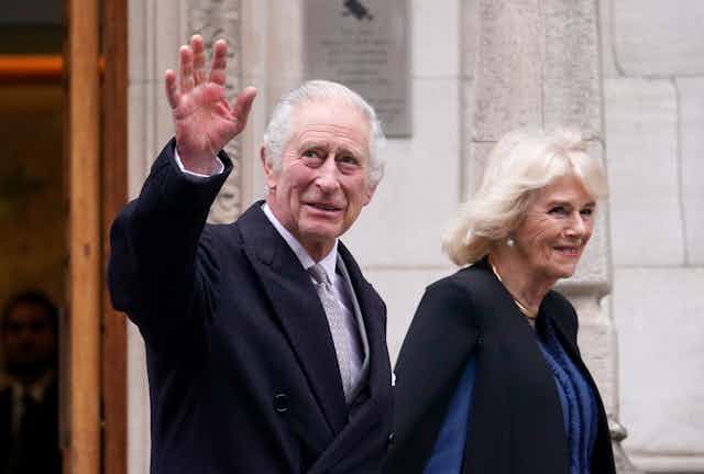 King Charles waving while walking next to Queen Camilla