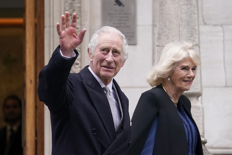 King Charles waving while walking next to Queen Camilla