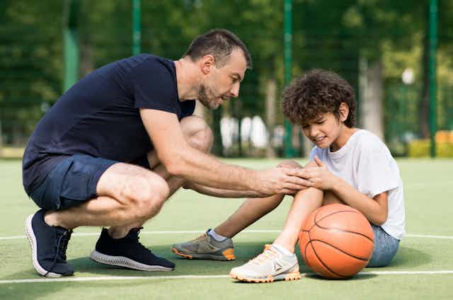 man checks injured child's knee on basketball court