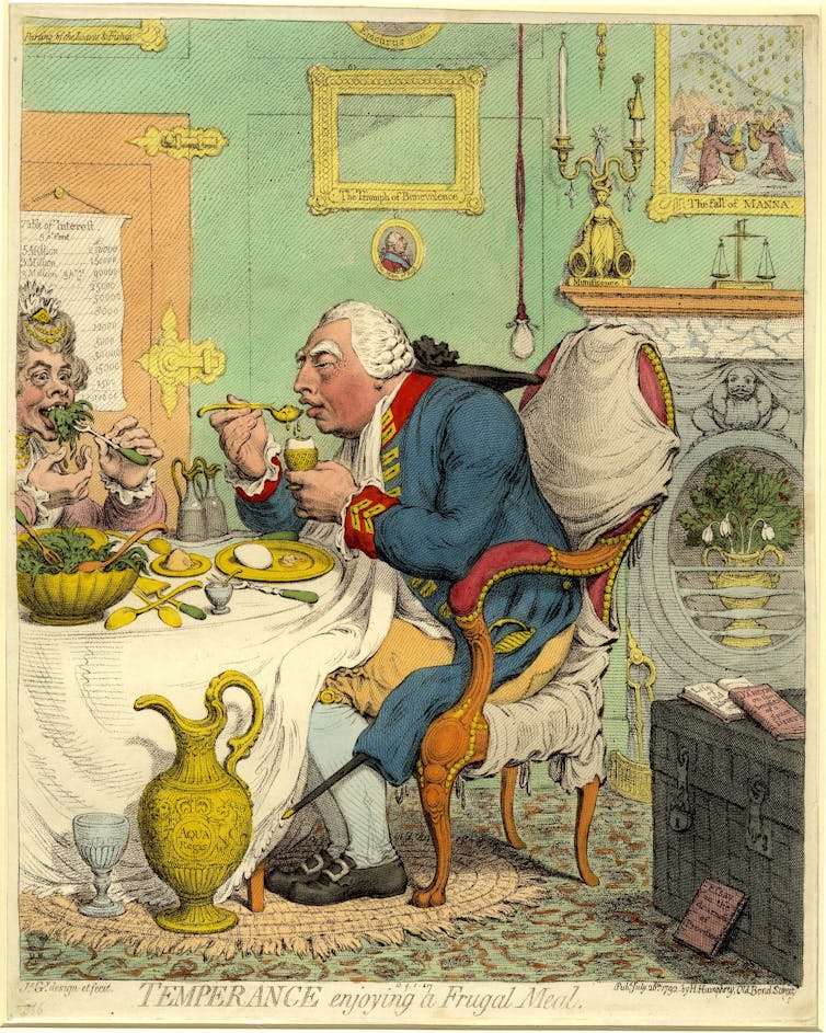 O Rei se senta em uma poltrona de perfil à esquerda, inclinando-se para a frente para comer um ovo cozido, segurando o copo de ovo em sua mão esquerda.