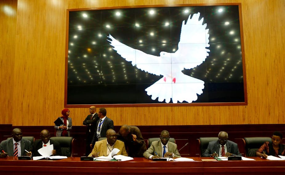 Five men and one woman signing documents with a large white bird on a screen behind them