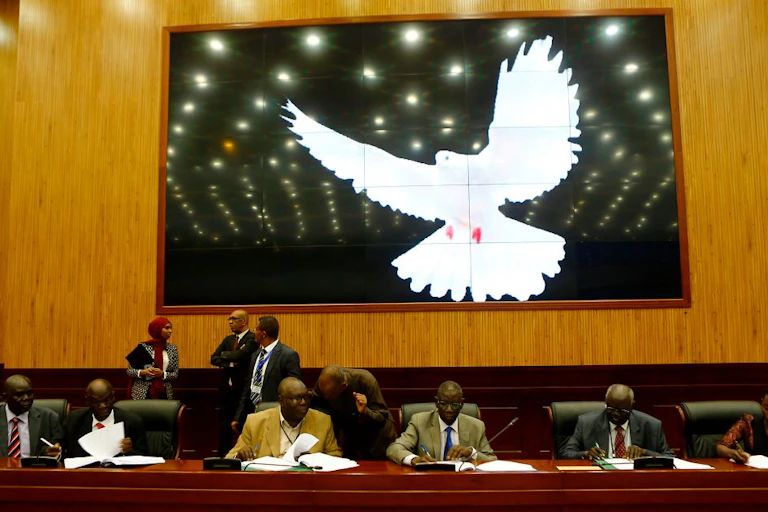 Five men and one woman signing documents with a large white bird on a screen behind them