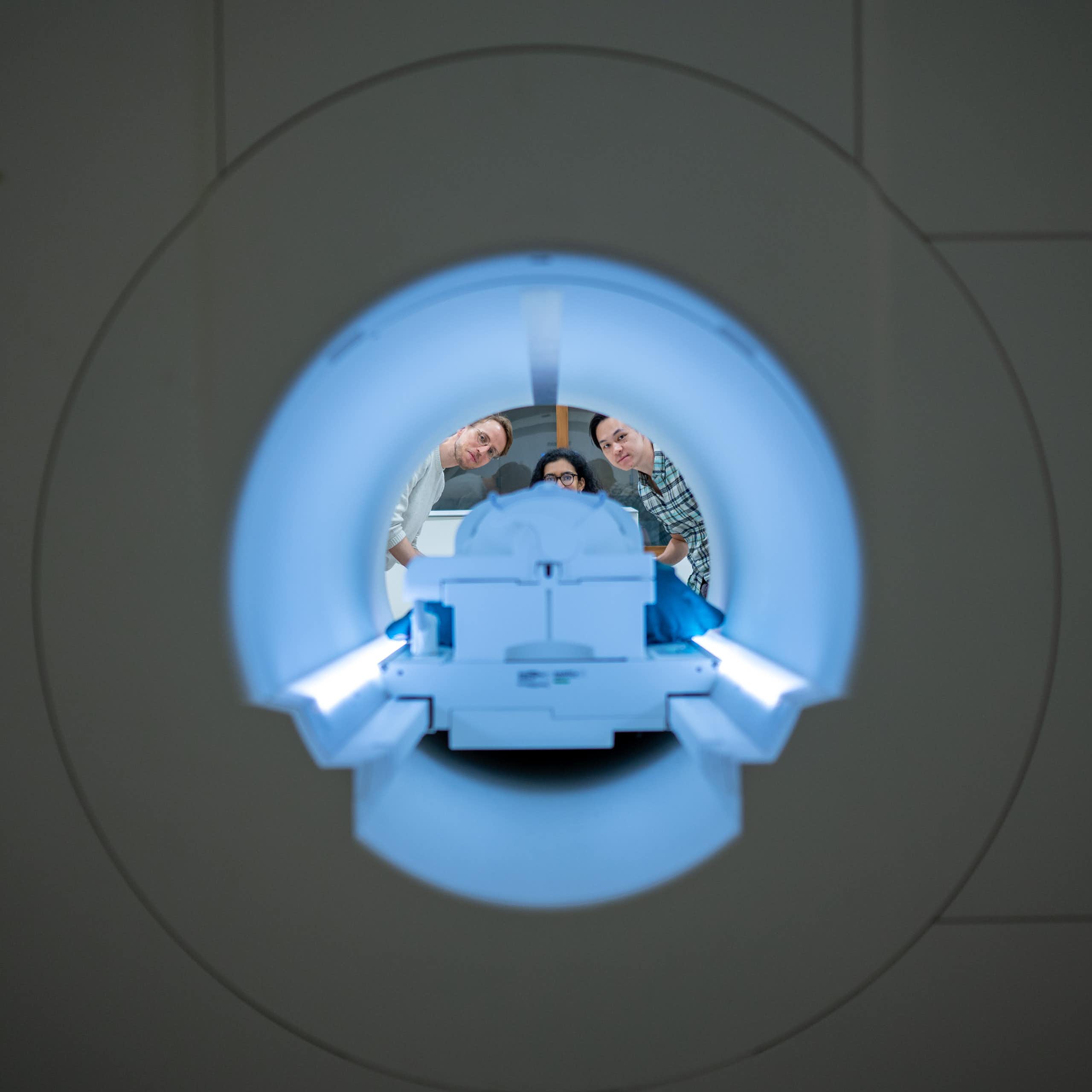 Three neuroscience researchers pose behind a large fMRI brain scanner