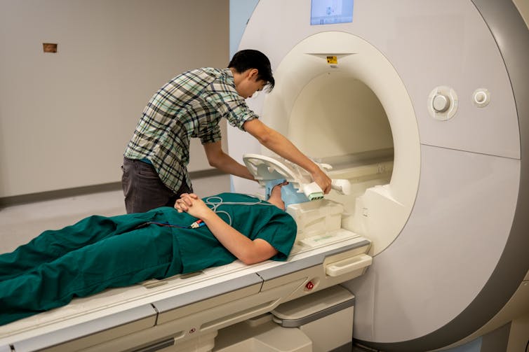 A researcher stands over a patient as they are about to enter an fMRI scanner
